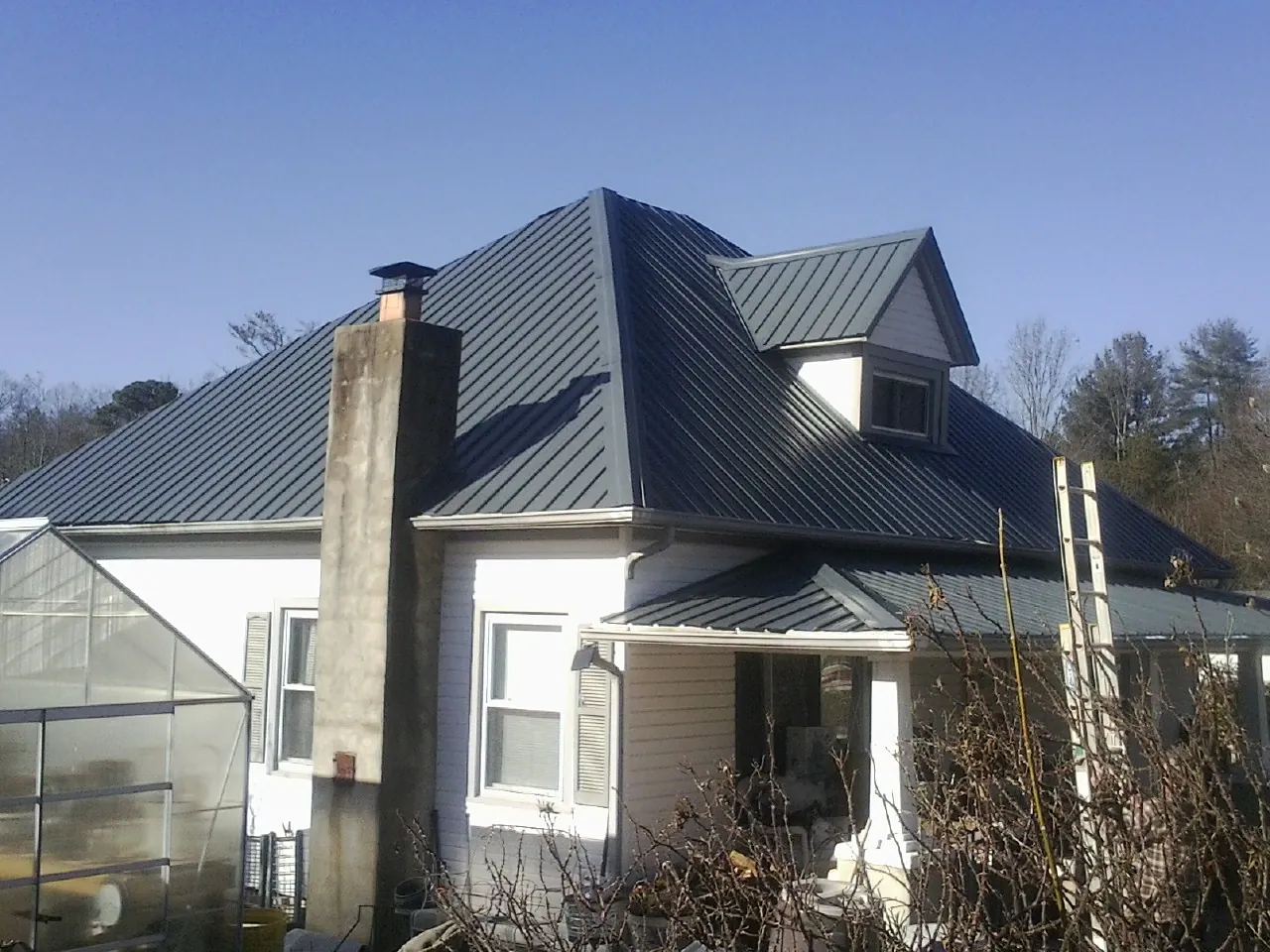 Dark blue standing seam metal roof on a white farmhouse with dormer — Slate & Tile Roof Repair by Roofing Brothers in Waunakee