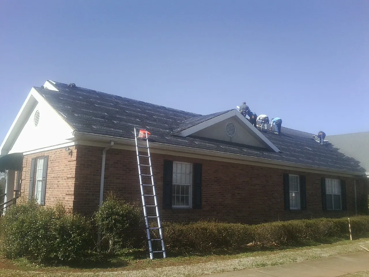 Crew tearing shingles off a brick ranch roof with a ladder set — Emergency Roof Repair work by our crew in Waunakee