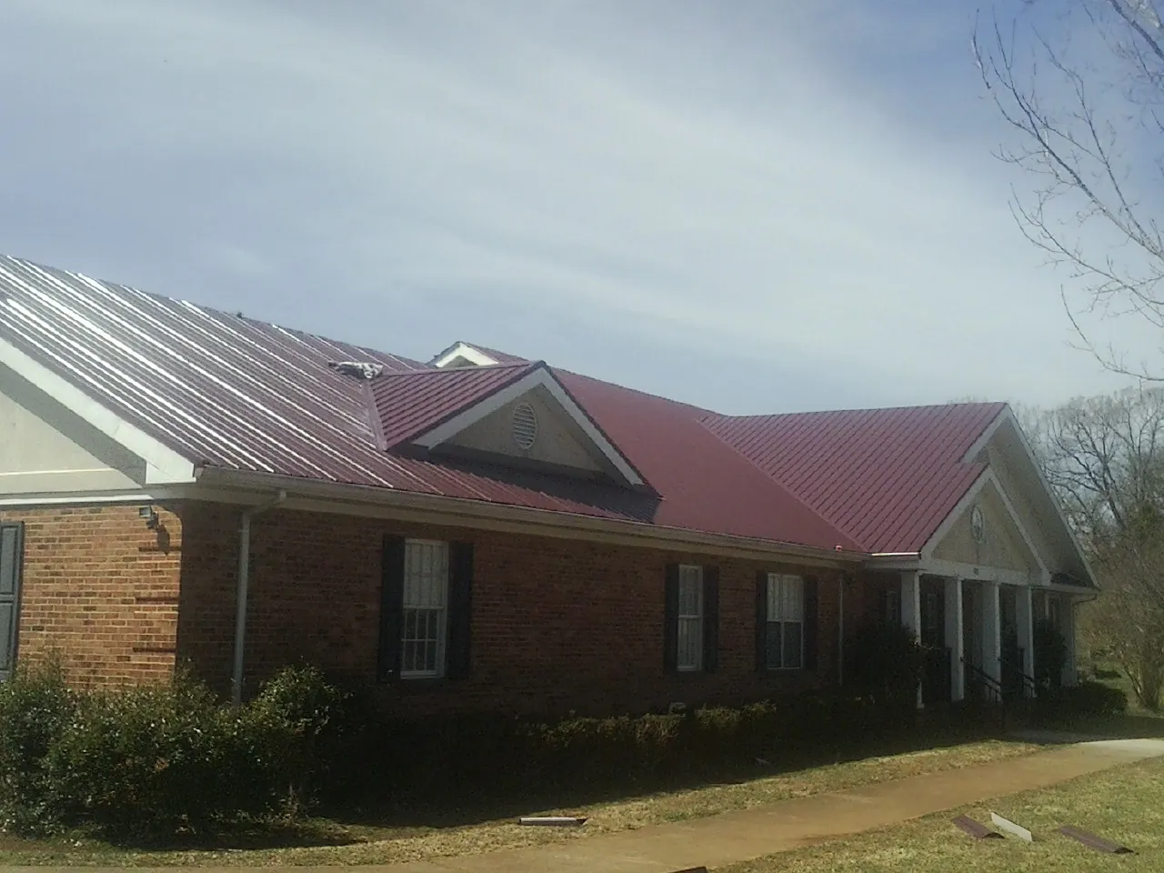 Red metal roof with gabled entries on a long brick building, from a Hail Damage Roof Repair job in Waunakee
