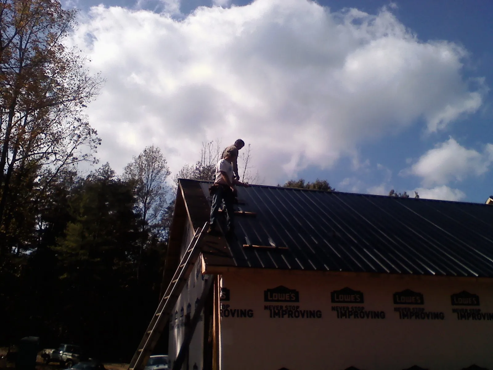 Roofer fastening dark metal panels high against a cloudy sky, from a Roof Inspection job in Waunakee