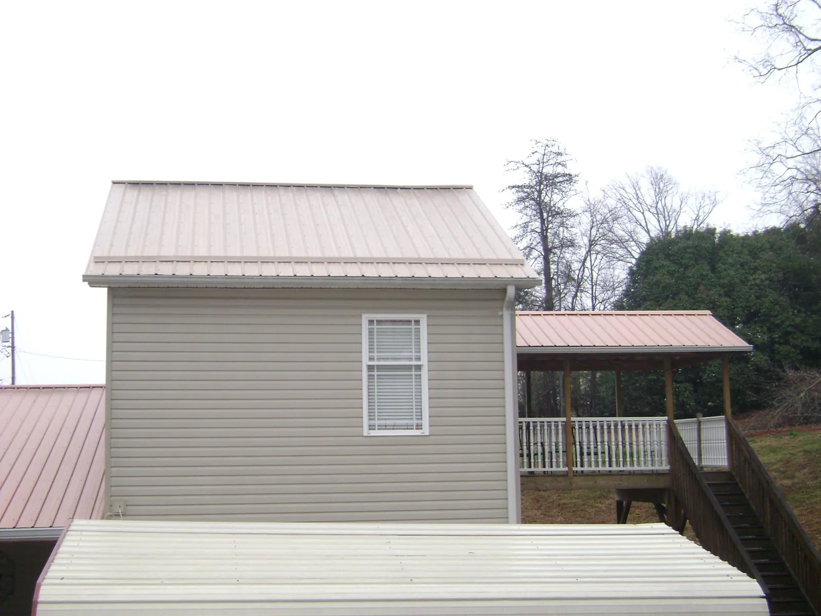 Tan metal roofs on a two story addition and attached porch, from a Roof Replacement job in Waunakee